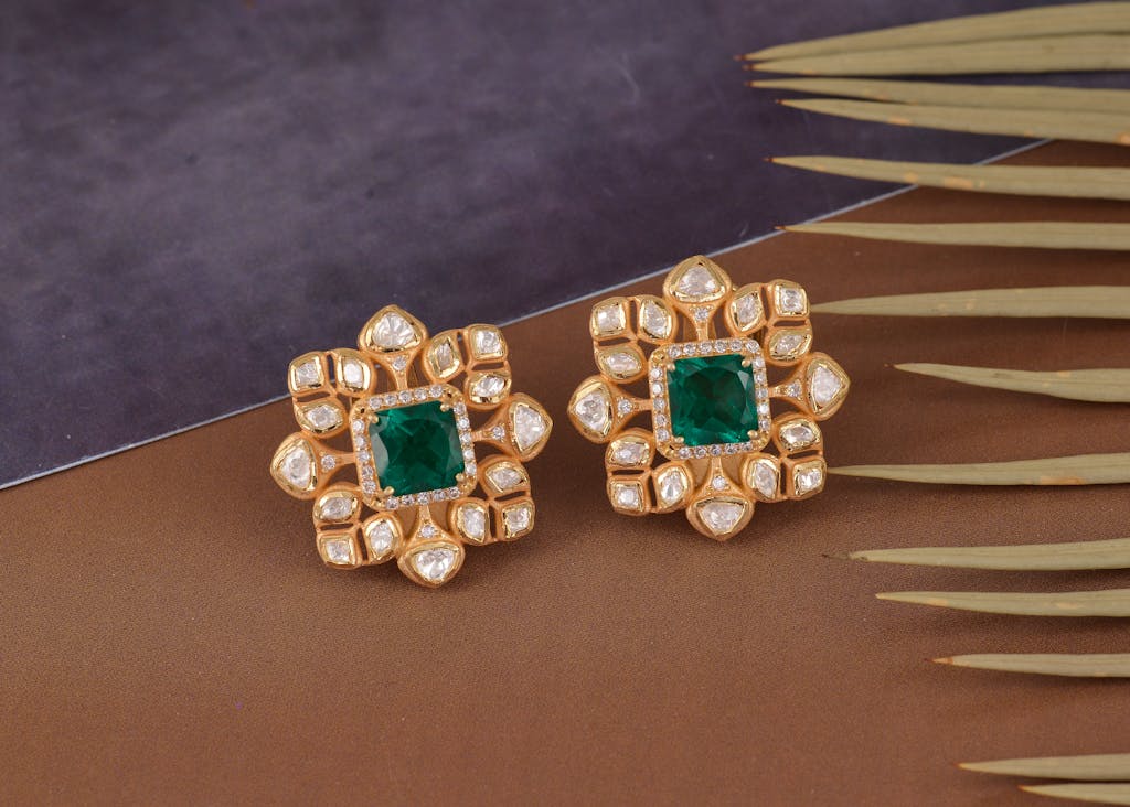 Luxurious gold earrings featuring emerald and diamond accents in a stylish design.