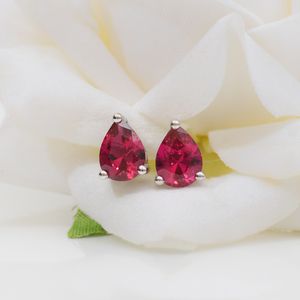 Glamorous pear-shaped ruby earrings displayed on a white flower backdrop, highlighting elegance and sophistication.